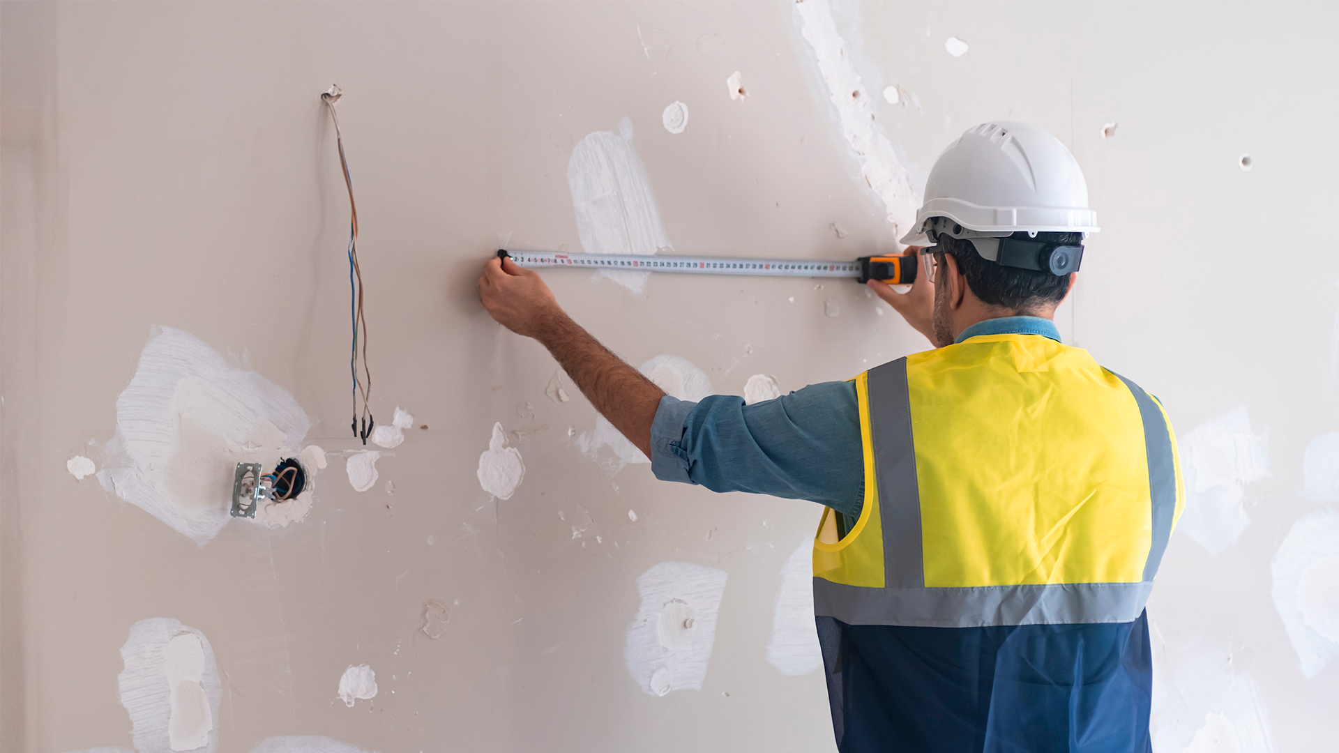 Trabajador de construcción mide pared de gypsum durante proceso constructivo. IPCONS. Agosto 2023.