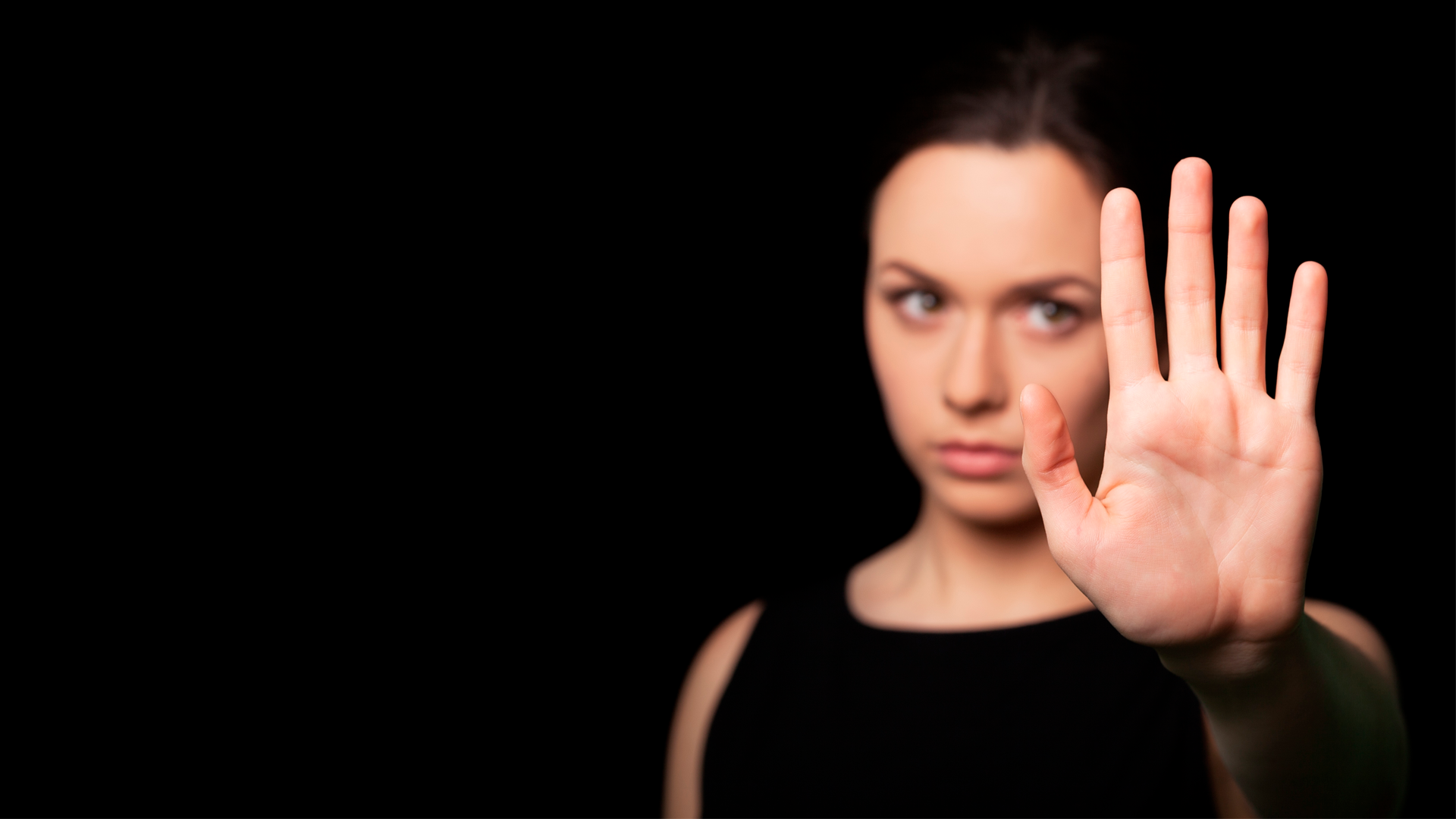 Mujer joven sostiene la mano al frente en señal de alto. Día Internacional de la Eliminación de Violencia contra la Mujer 2023.