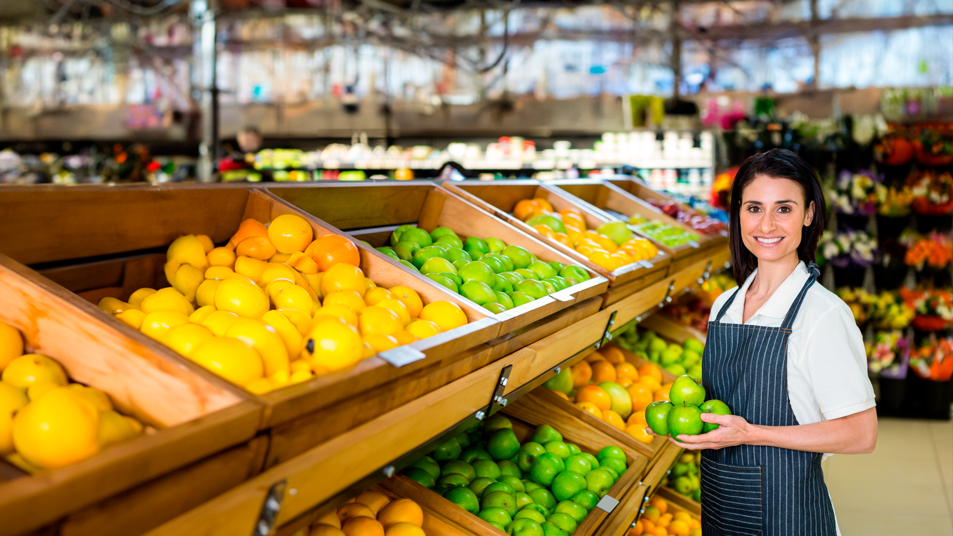 Mujer trabajadora de la industria de servicios acomoda fruta en estante de supermercado. ENADEL 2024. Salida a campo.