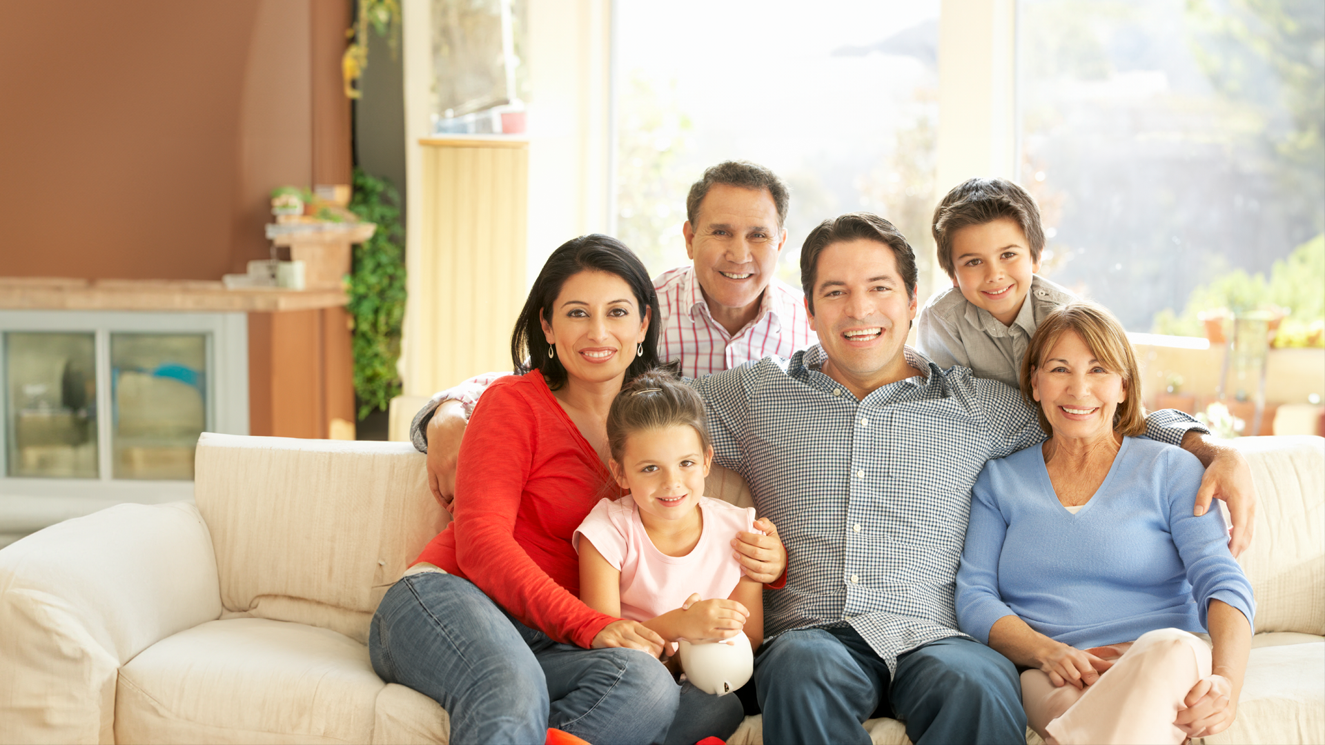 Familia de seis miembros sonríe a la cámara mientras posan sentados en un sofa en la sala de sus casa. ENAHO 2024. Inicio.