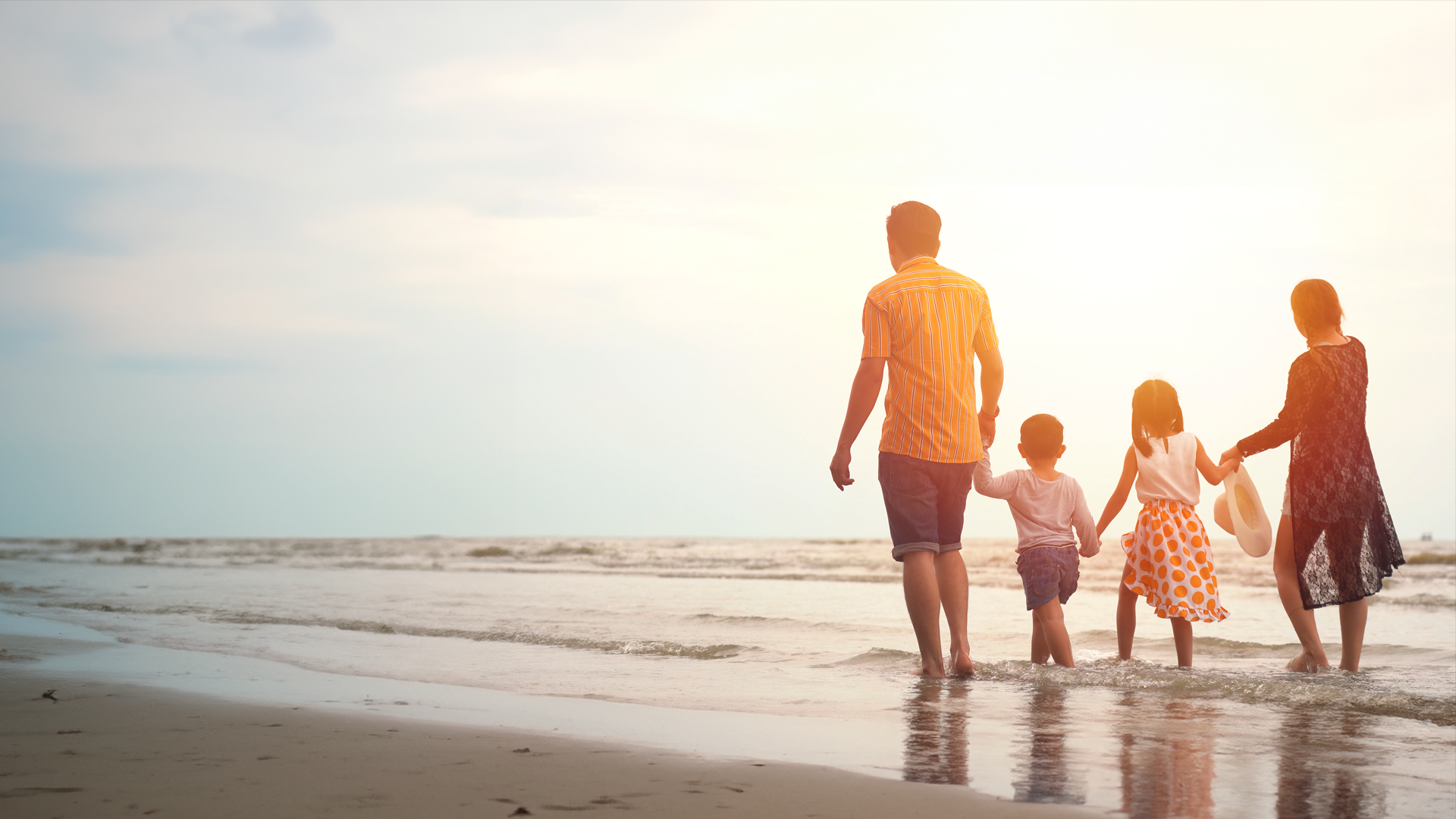 Familia de cuatro personas camina en la playa a la orilla del mar durante el atardecer. IPC. JUN 2024.