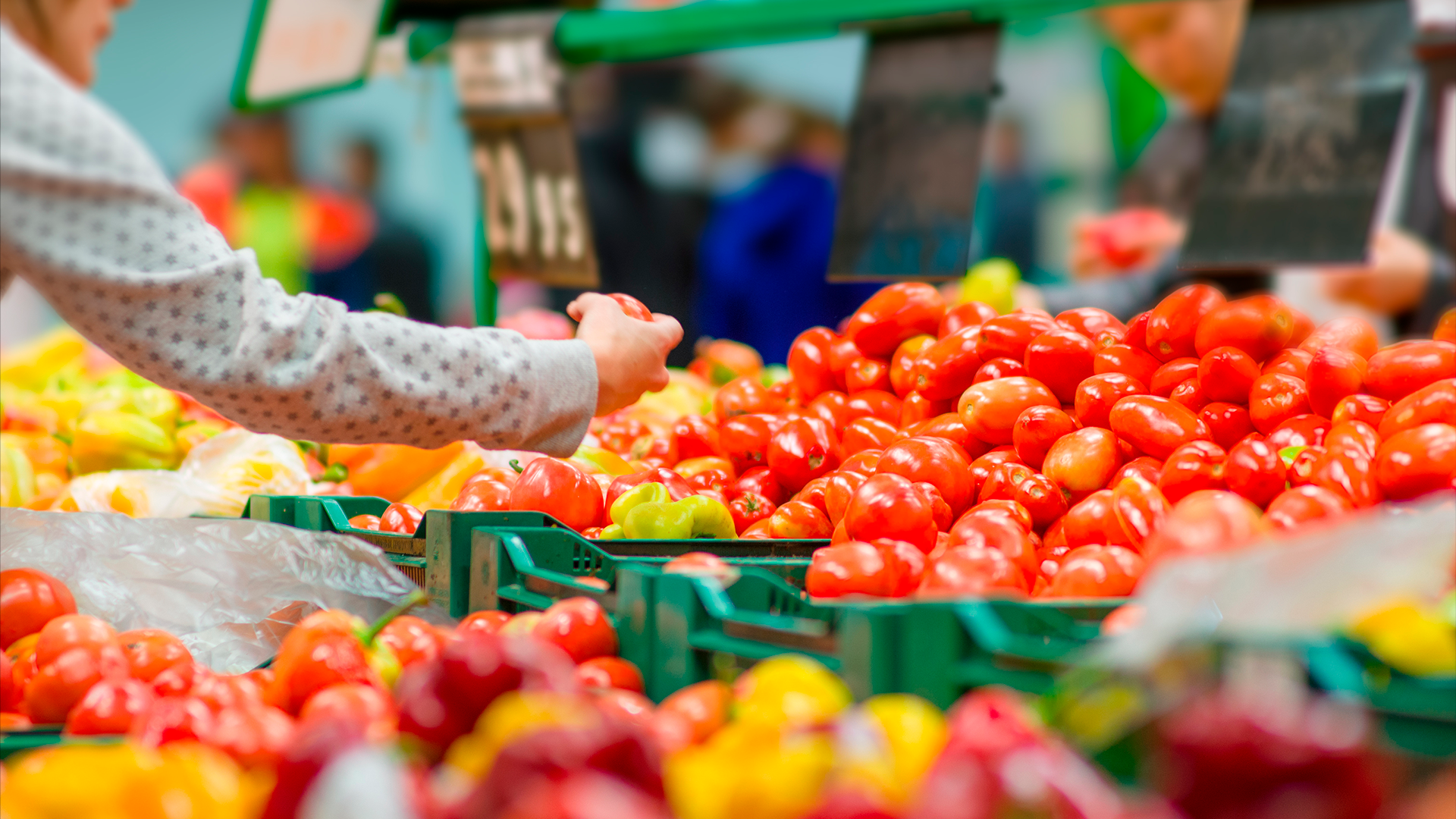 Mano de mujer sostiene tomate en sección de verduras del supermercado. IPC. AGO 2024.