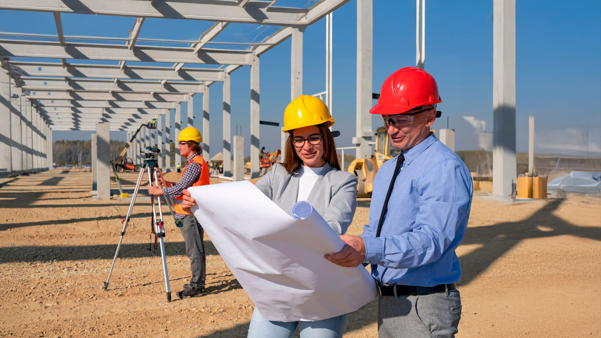 Arquitecta y arquitecto revisan plano en obra de construcción comercial durante día soleado. Estadísticas de la Construcción. Cifras anuales preliminares 2024.