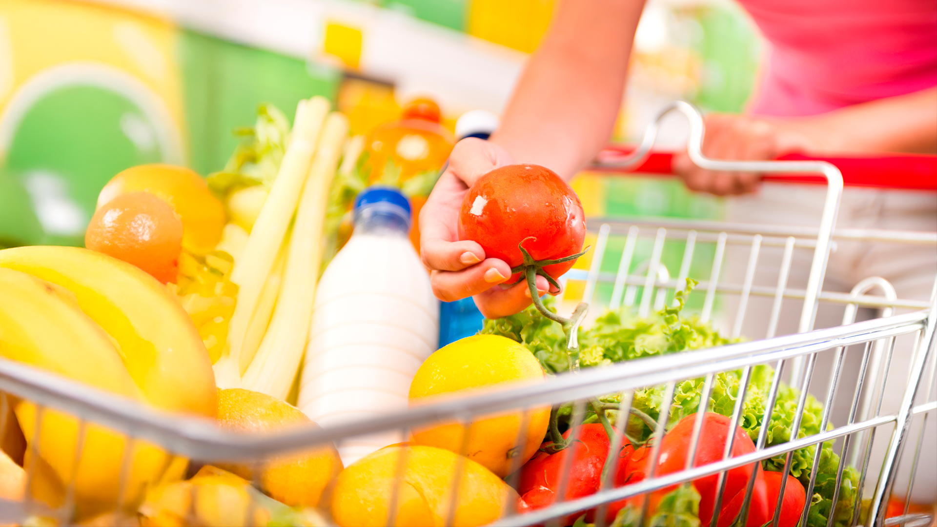 Detalle de mano de mujer sosteniendo tomate sobre carrito de compras en supermercado. IPC. JUN 2025.