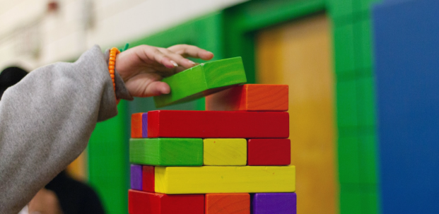 bloques de madera color amarillo, rojo, verde, azul y naranja en forma de torre con una mano