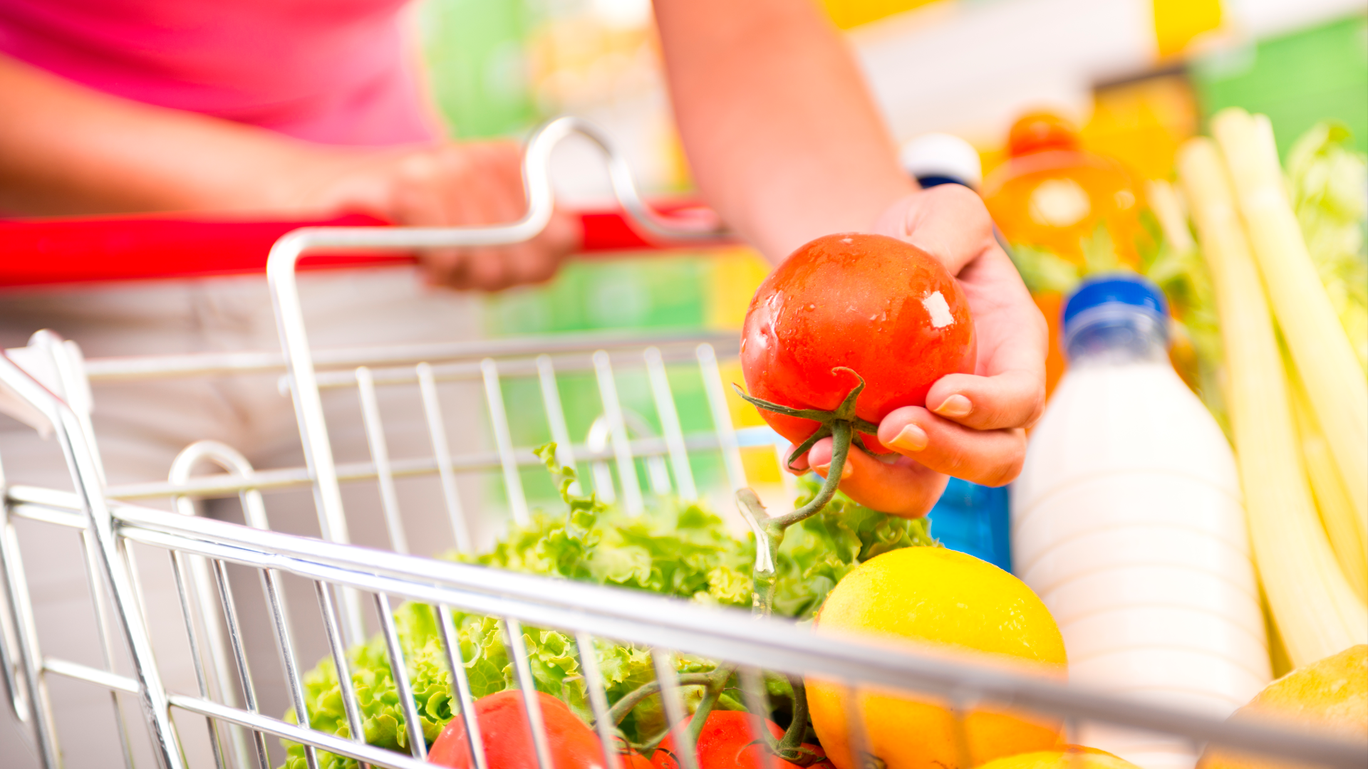 Foto de detalle. Mano de mujer sostiene tomate sobre carrito de compras con víveres en supermercado. ECE. MAR 2024.